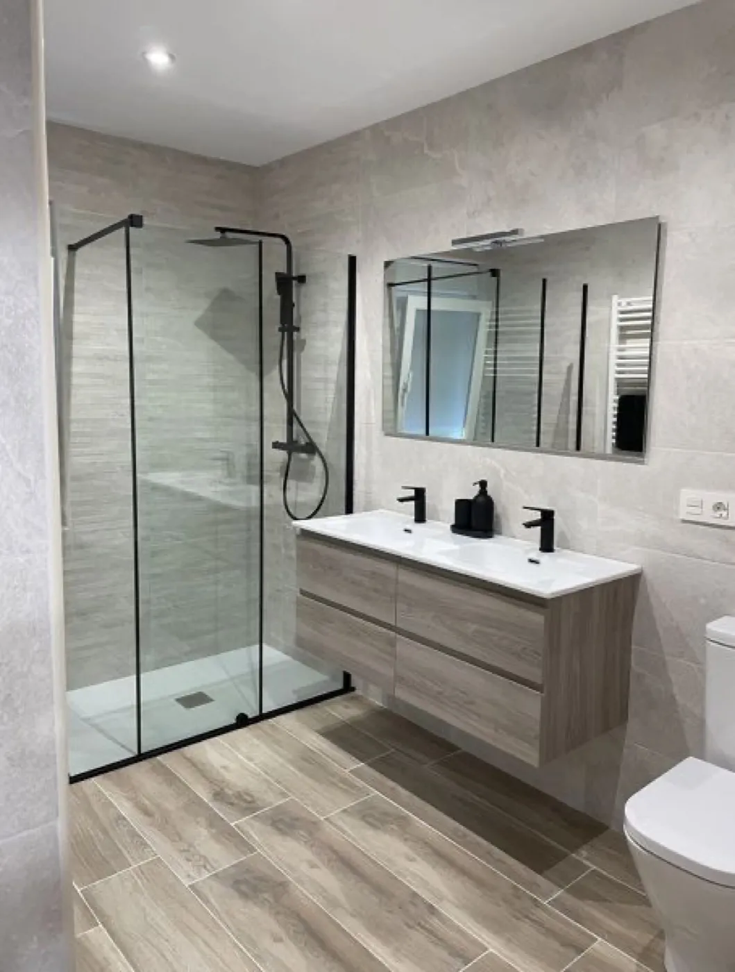 Baño reformado en Marbella con doble lavabo, mampara negra y acabados de calidad
