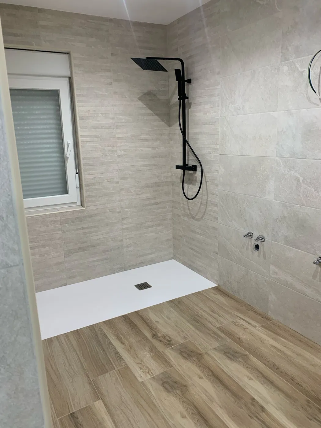 Reforma de baño con ducha walk-in, grifería negra y suelo porcelánico imitación madera